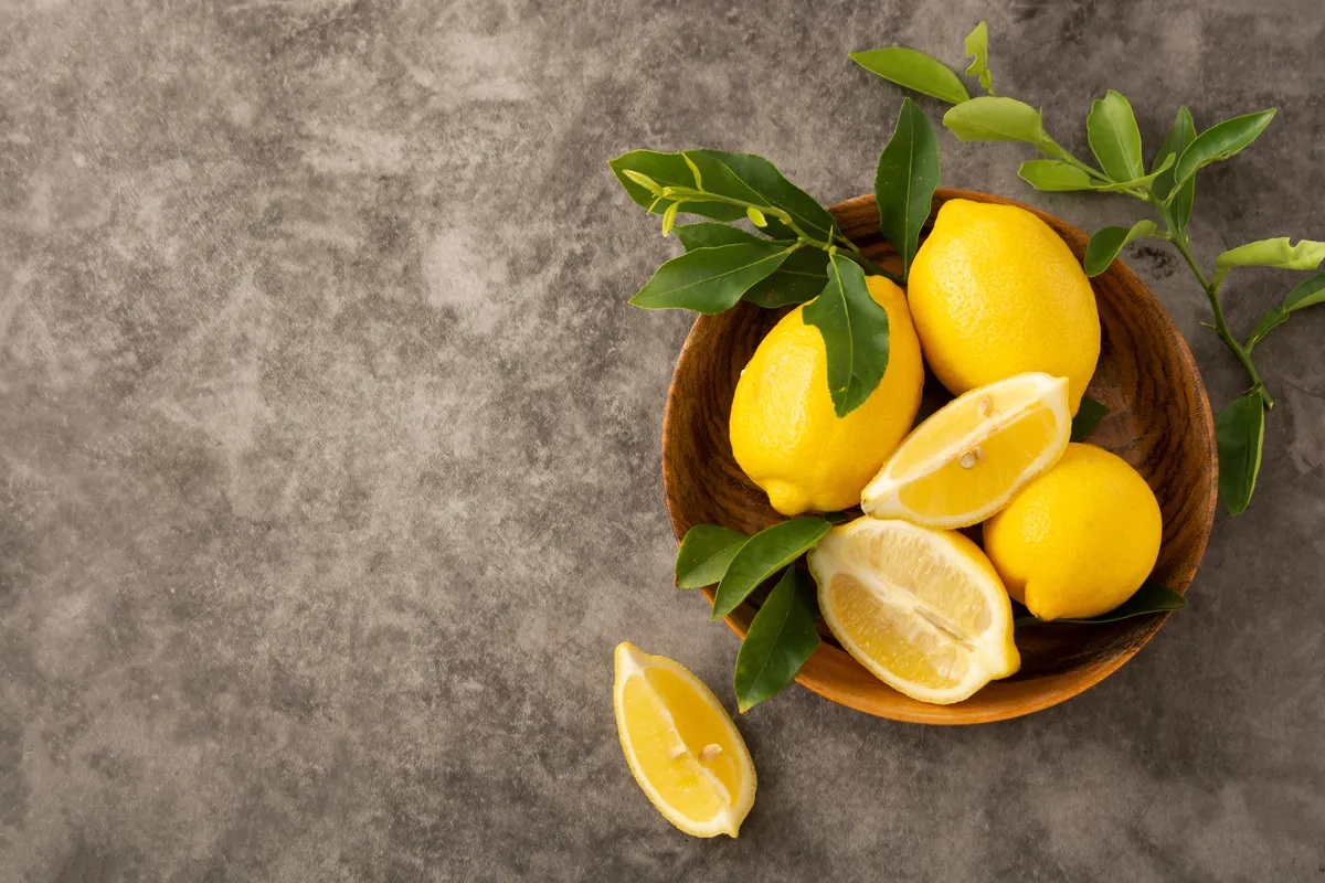  a bowl of lemons with leaves on the table