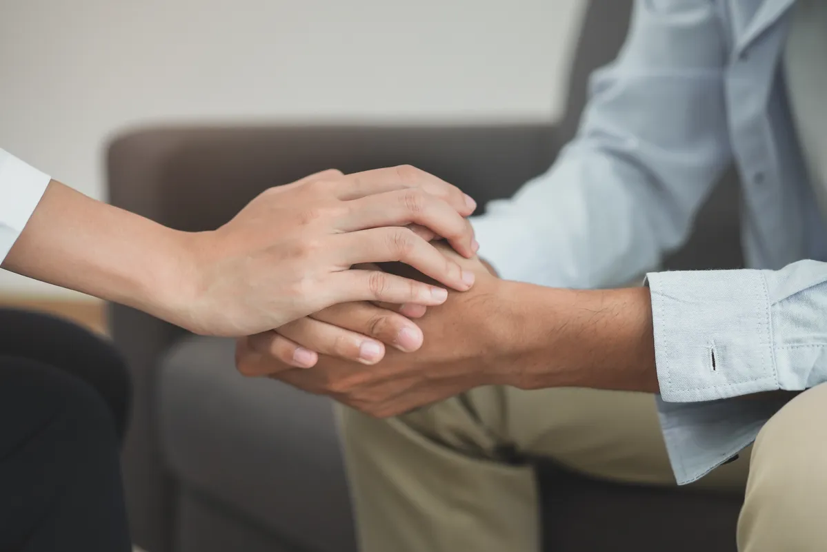 someone holding the hand of a man who is sitting on a couch