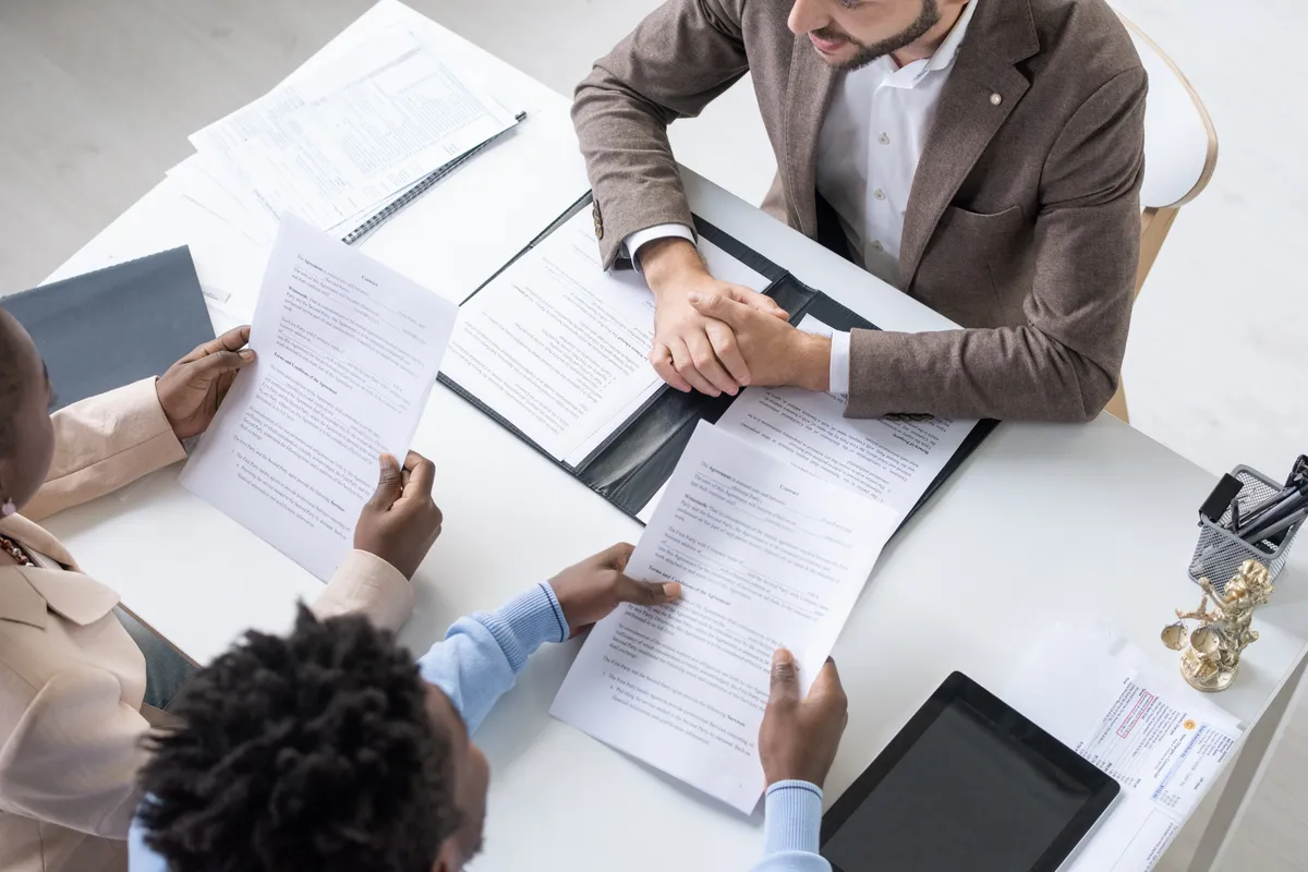  two men shaking hands over a table with papers