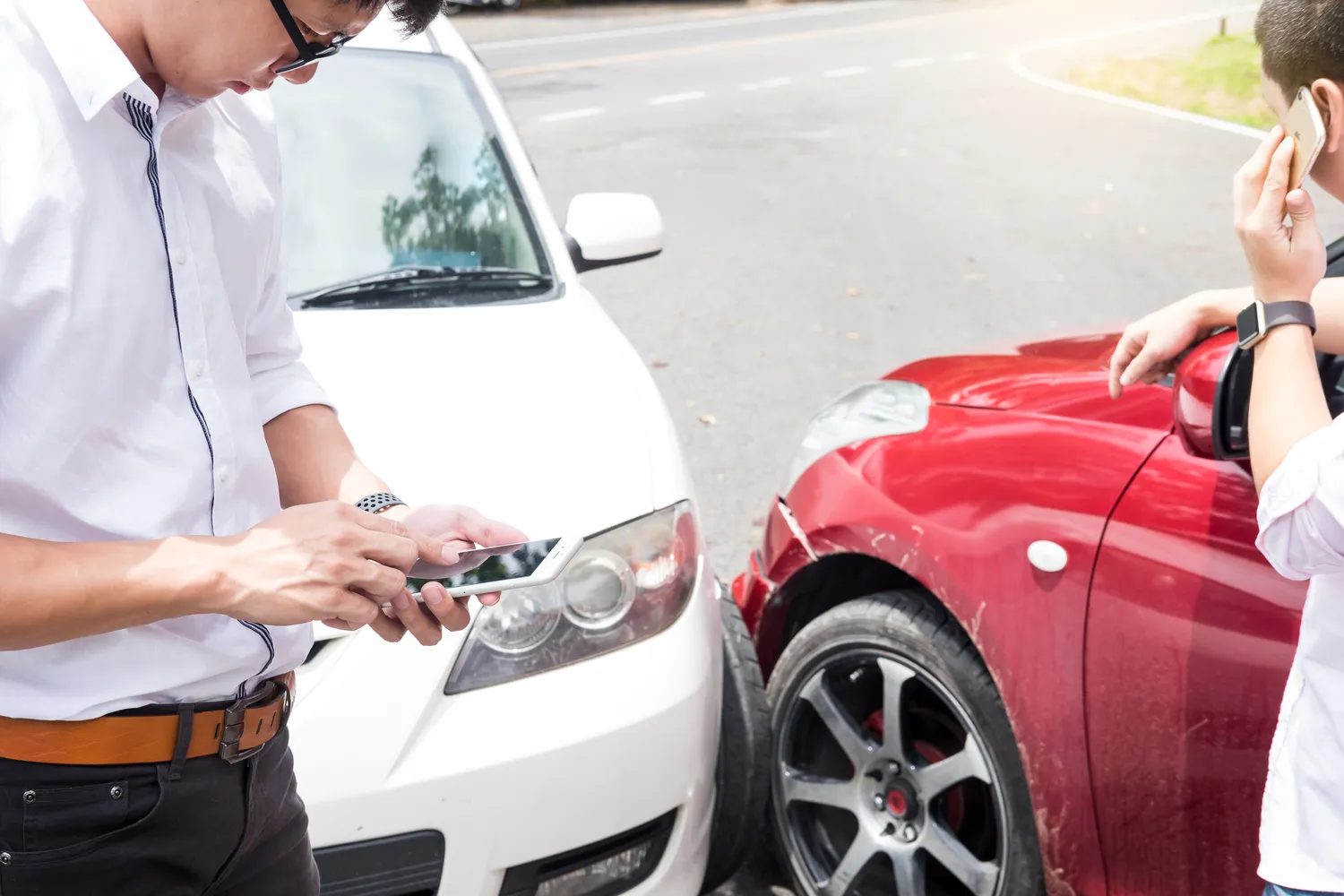 Two people talking on their phones after a car accident.