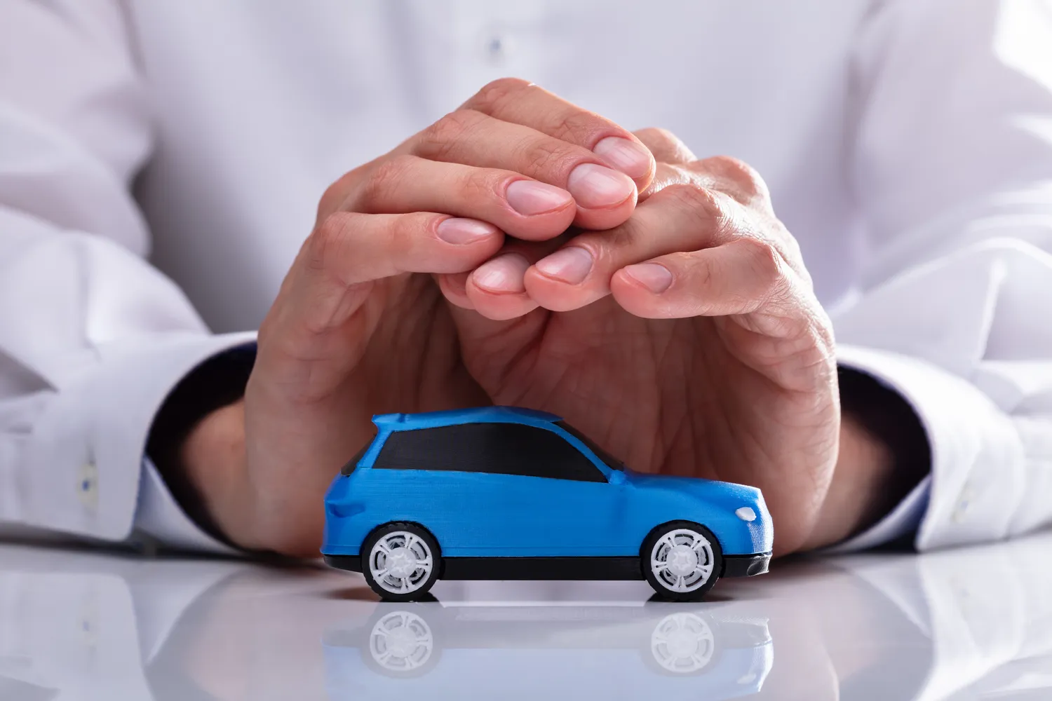 Insurance agent protecting a blue toy car with their hands